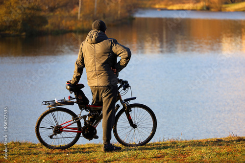 Man stopped with bicycle on lake and autumn forest background. Cycling, travel and leisure in fall season