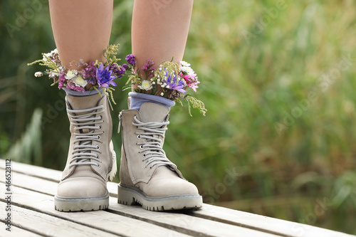 Woman standing on wooden pier with flowers in socks outdoors, closeup. Space for text photo