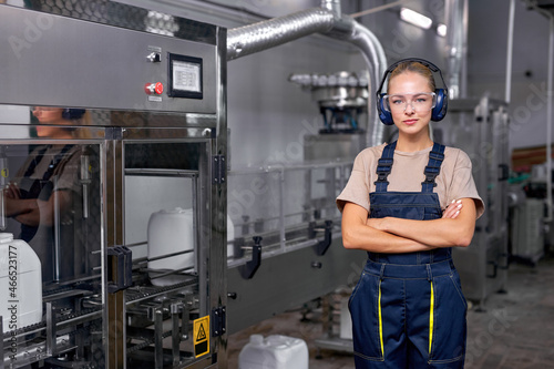Confident caucasian industrial female engineer in spectacles standing in factory at work place, dressed in blue uniform. pesticides production in factory. female engineer look at camera, posing