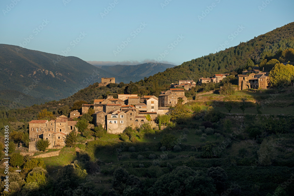 Village typique avec maisons de pierre dans le soleil levant accroché au flanc de la montagne avec château fort en ruine sur la crête.