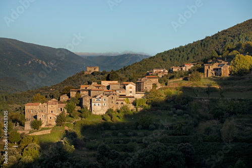 Village typique avec maisons de pierre dans le soleil levant accroché au flanc de la montagne avec château fort en ruine sur la crête.