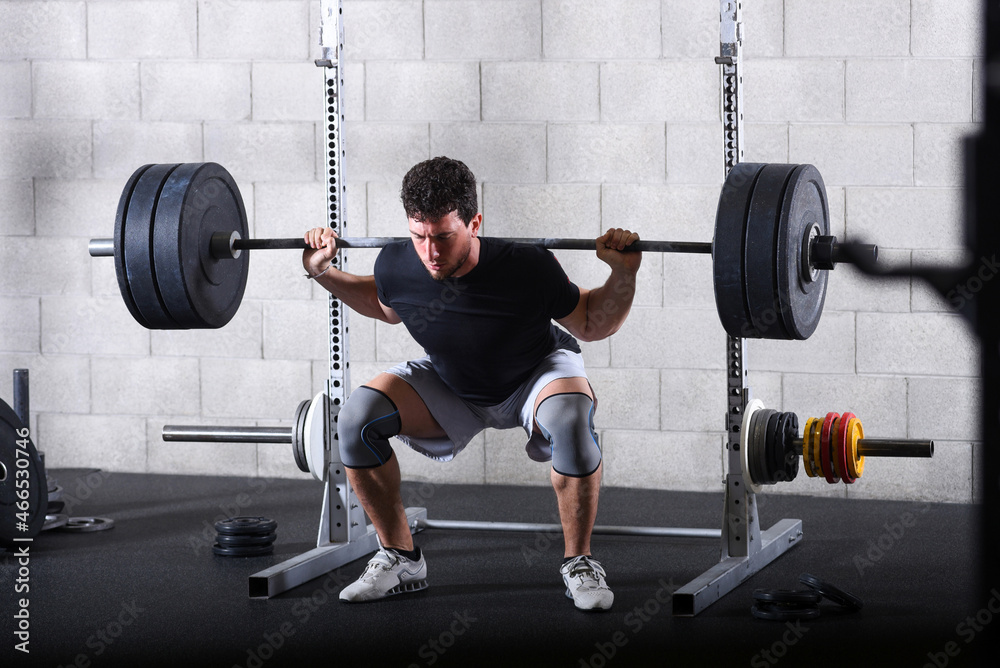 Young man performing heavy back squats exercise in gym Young man performing heavy back squats exercise in gym