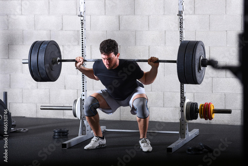 Young man performing heavy back squats exercise in gym