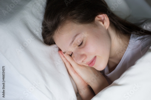 Dreaming girl lying on white bed with pillow, enjoying free time at weekend