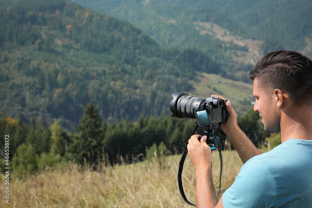 Professional photographer taking picture with modern camera in mountains. Space for text