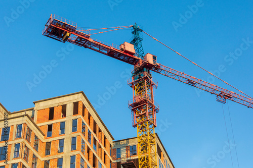A tall construction crane is working on building a house