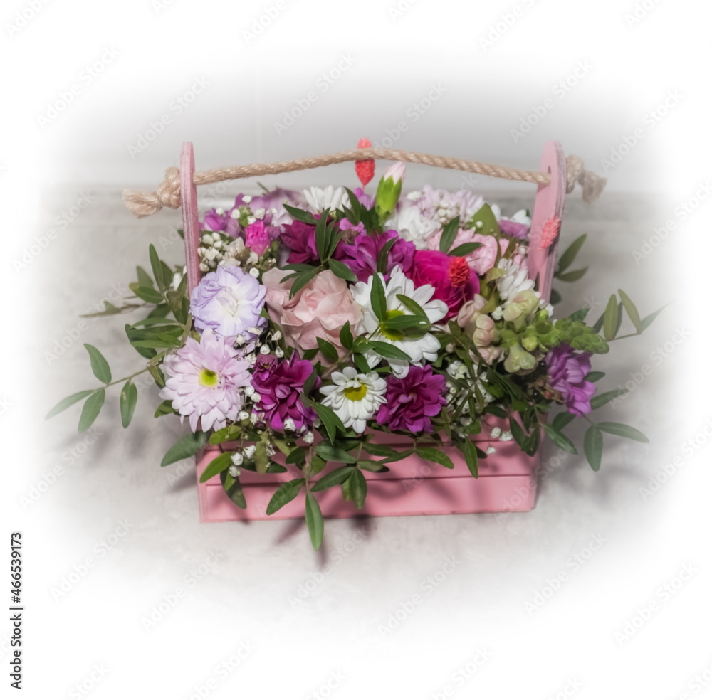 Multicolored flowers of roses and chrysanthemums close-up in a pink wooden basket on a white background