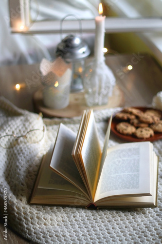 Plate of chocolate chip cookies  cinnamon sticks  soft blanket  open book and lit candles. Hygge at home. Selective focus.