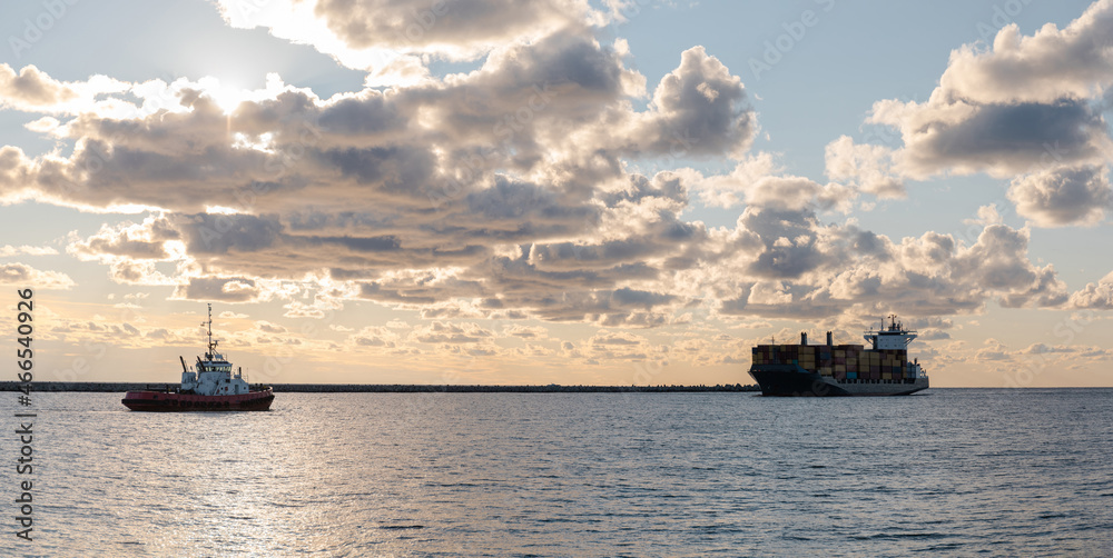 tugboat meets a large commercial cargo ship in the port against the backdrop of sunset, panorama