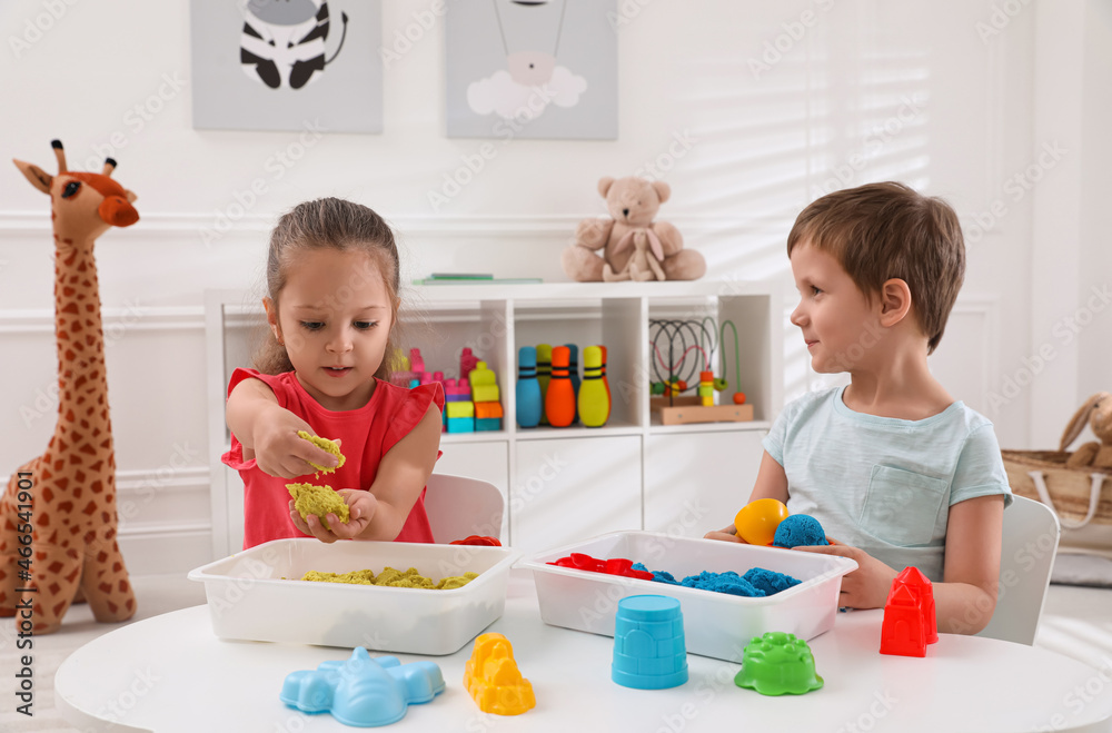 Cute little children playing with bright kinetic sand at table in room