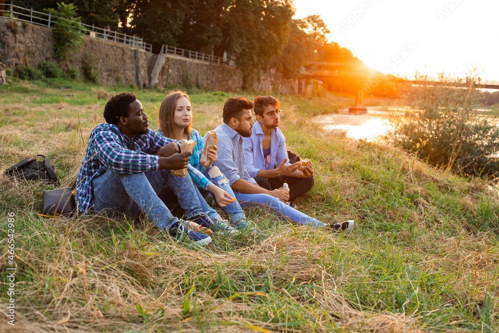 The group of young diverse people eating fastfood on nature