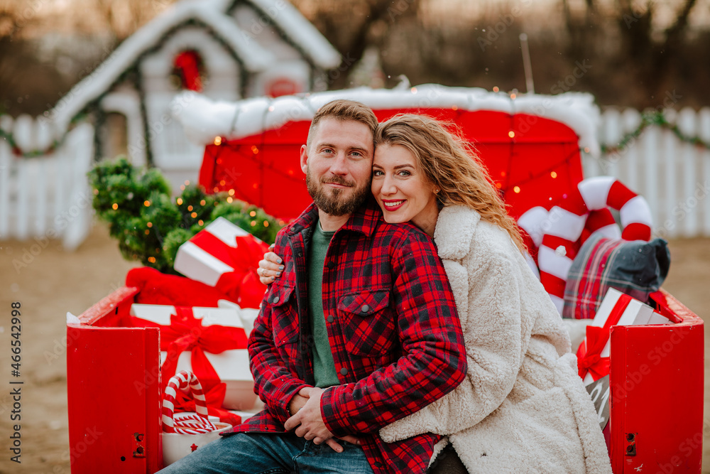 Young happy couple in winter clothes posing in Christmas car under the snowing.