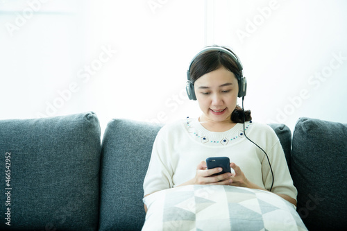Asian young woman relaxing in living room and enjoy listening a musing on smartphone.