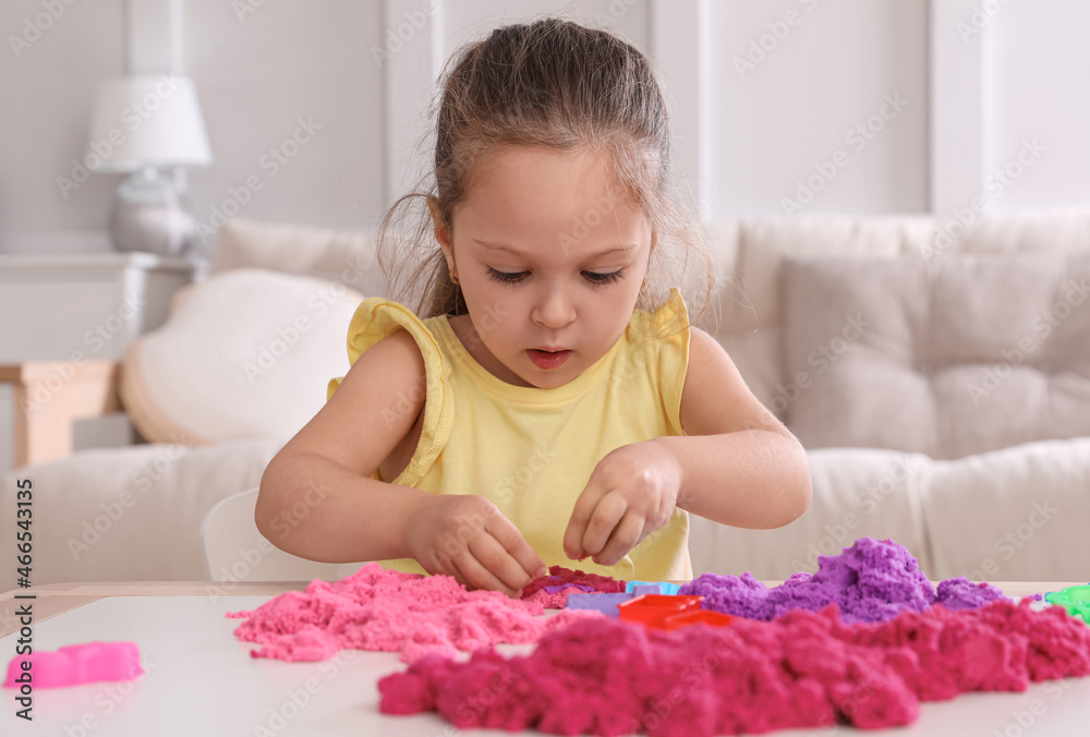 Cute little girl playing with bright kinetic sand at table in room Cute little girl playing with bright kinetic sand at table in room