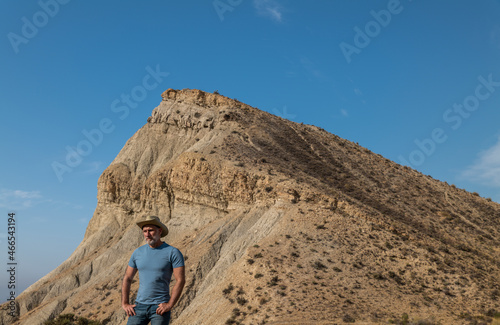 Portrait of adult man in cowboy hat in desert area against mountain and blue sky