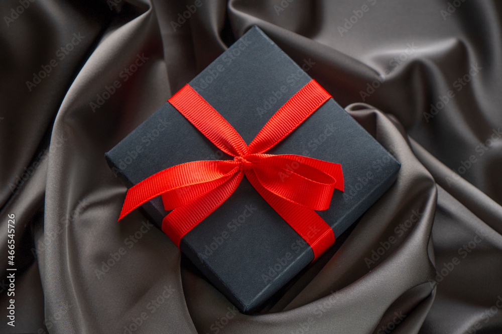 Black gift box with red bow ribbon on the satin cloth. Black gift box with red bow ribbon on the satin cloth.