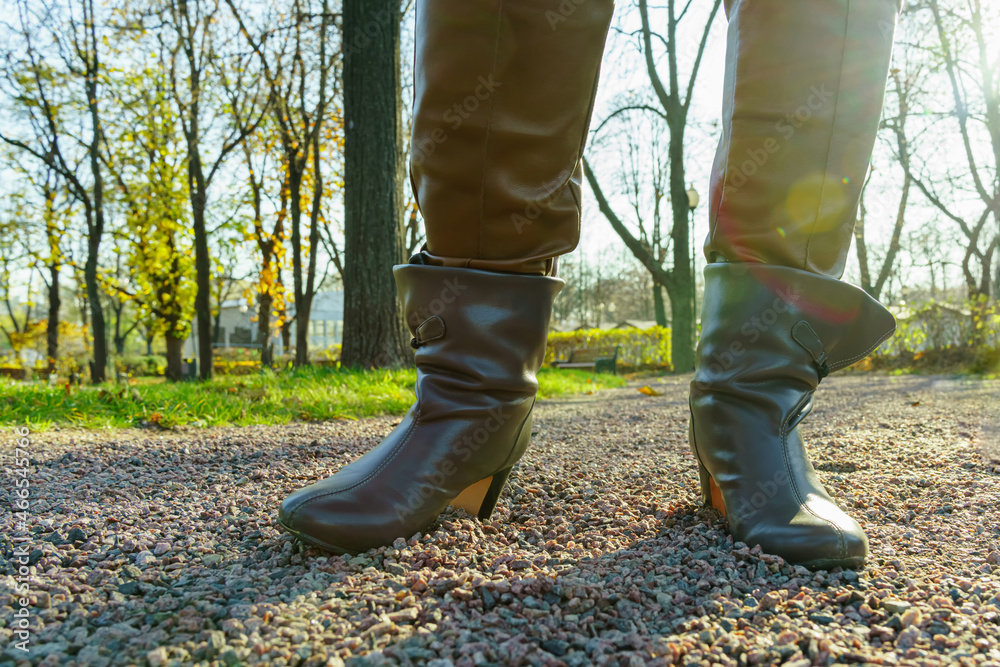 Chubby women's legs in brown leather pants and gray boots.