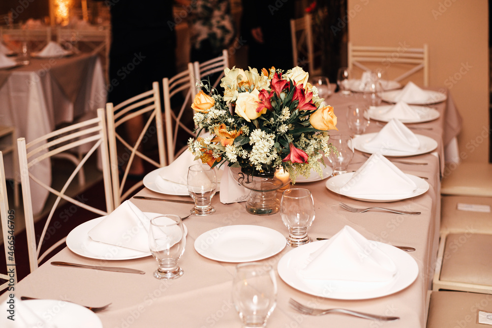 wedding decoration - table set with plates, cutlery and glasses with white, yellow and orange flowers
