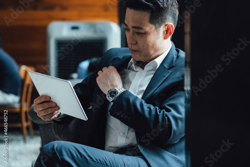 Handsome Asian Businessman Using Digital Tablet in a Cafe. Serious business man in blue suit watching or reading something on a digital tablet while sitting in a restaurant.