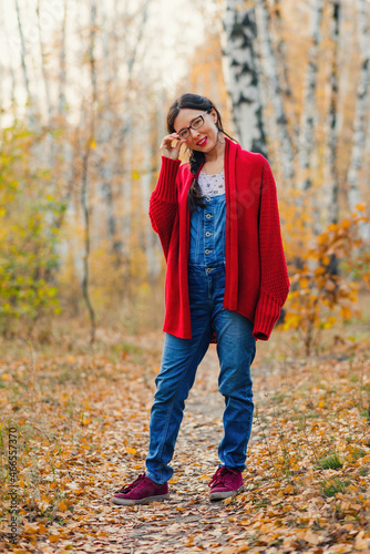 woman in glasses stands and looks at the camera on the background of the autumn forest