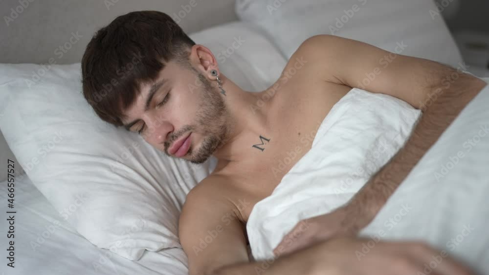 Portrait of handsome bearded millennial man sleeping in white cozy bed at home. Happy relaxed Caucasian man with closed eyes lying in comfortable bedroom indoors. Leisure and resting