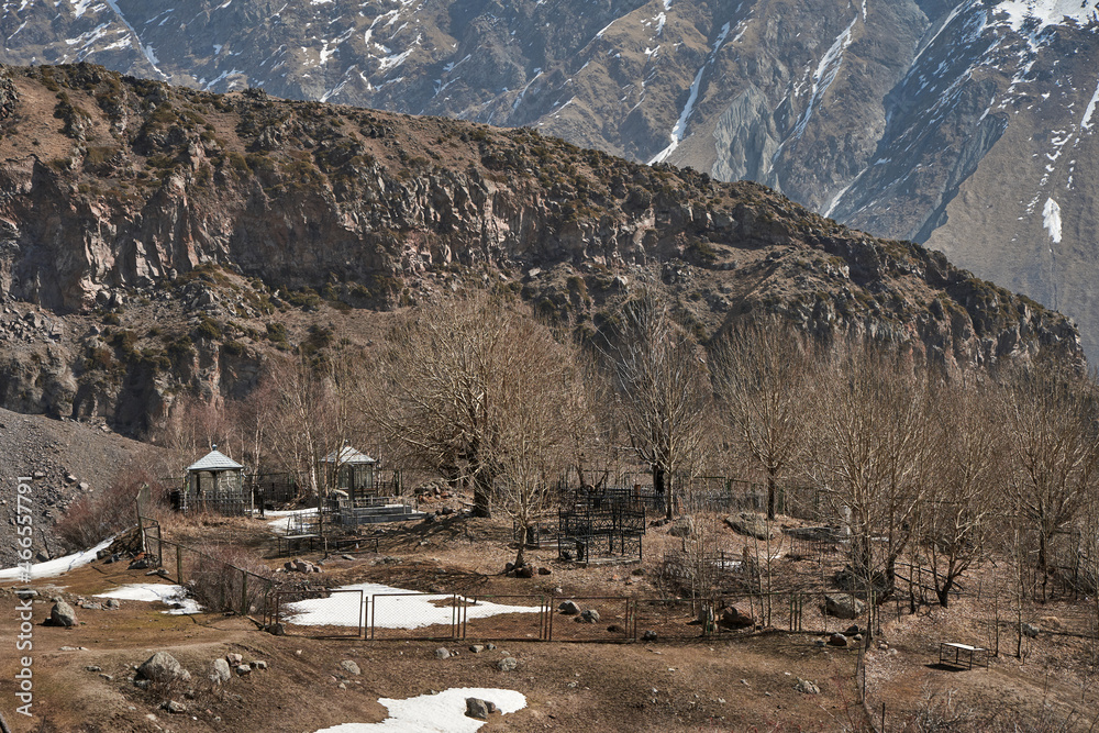 A cemetery on a hill in a mountain valley. High snow-capped mountains in the background