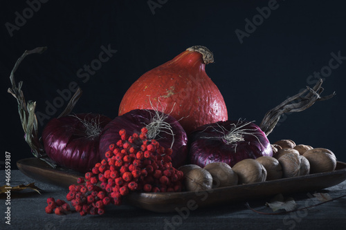 Pumpkin, onion, nuts and rowan berries on a wooden plate. Autumn harvest. Samhain.