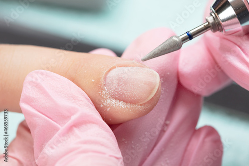 Removing the nail plate with a milling machine. Manicure process in beauty salon, cleaning of nails by a milling cutter. Manicurist filing client's nails at table, close up. Shallow depth of field