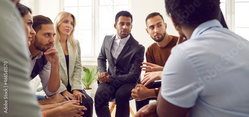 Young diverse business team talking during work meeting. Banner with group of serious multiracial multiethnic people sitting in circle, discussing important things, listening to colleague's suggestion