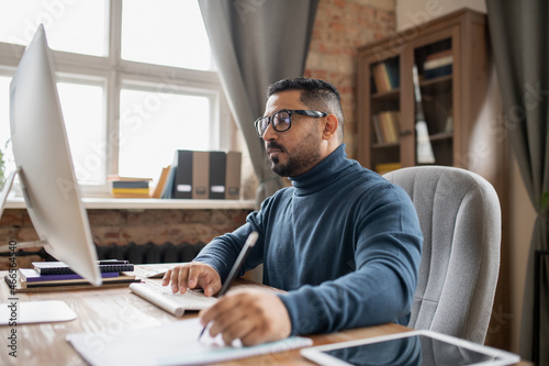 Serious mature man pressing key and looking at computer screen while making notes during online lecture