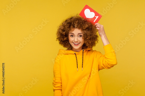 Optimistic woman blogger posing with positive expression  recommending to follow and share blog with trendy content  wearing casual style hoodie. Indoor studio shot isolated on yellow background.