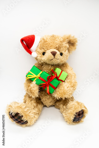 Vertical photo with stuffed toy Teddy bear in a red Santa Claus hat with a pompom on one ear, holding green gift boxes in its paws. White background, copy space. The concept of Christmas gifts, sales © Yulia