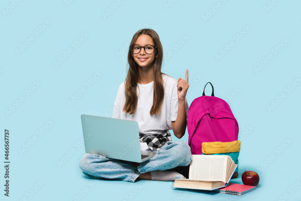 Sitting full-length teenager schoolgirl with laptop computer showing pointing on copy space having idea, surfing webpages on Internet,social media,e-learning remotely isolated in blue background - obrazy, fototapety, plakaty 