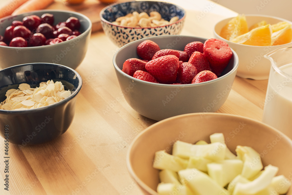 Group of bowls with fresh cherries, strawberries, juicy oranges, almond flakes, cashew nuts and milk for preparing homemade smoothie Group of bowls with fresh cherries, strawberries, juicy oranges, almond flakes, cashew nuts and milk for preparing homemade smoothie