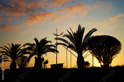 Evening sunset on the embankment of the resort town. A row of silhouettes of palm trees against the background of the burning sky