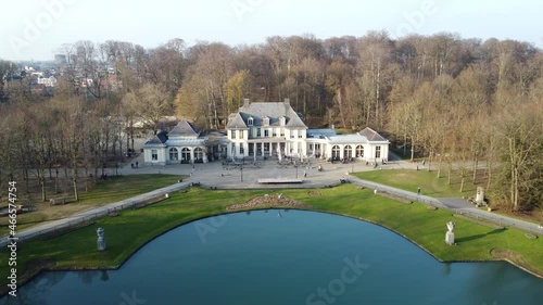 Aerial view of Rivierenhof castle in city park in Antwerp. Drone flying over the blue lake in autumn while people walking in front of the building photo