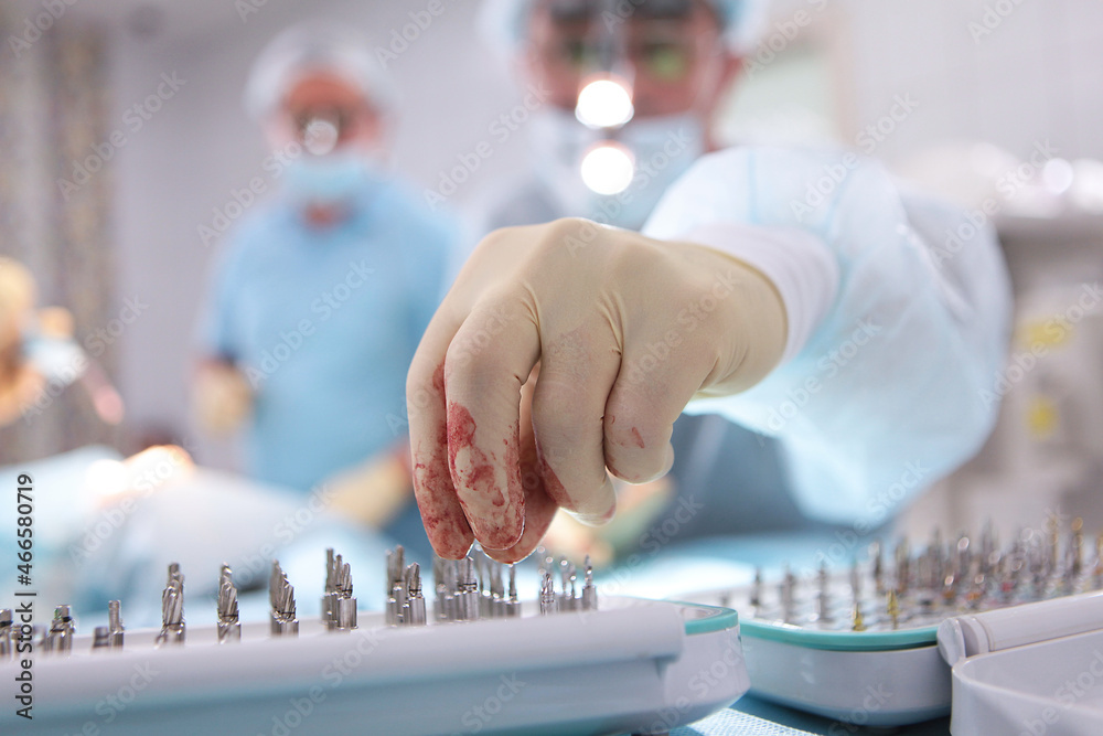 The dental surgeon selects the tips for installing the implants. Installation of implants in a modern dental clinic. Blood on the gloves. Only hands. Close-up. Copy space. The dental surgeon selects the tips for installing the implants. Installation of implants in a modern dental clinic. Blood on the gloves. Only hands. Close-up. Copy space.