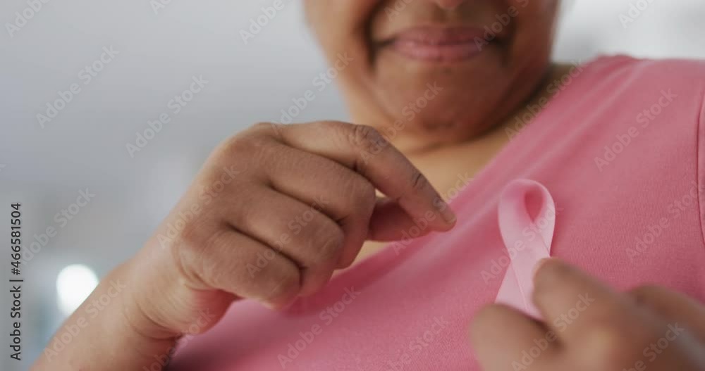 Midsection of smiling african american senior woman in pink t shirt and pink breast cancer ribbon
