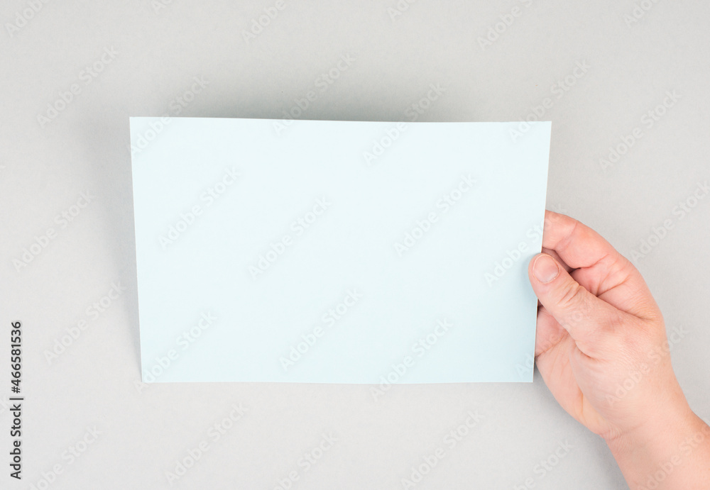 Woman holds a blank sheet of paper, grey colored background, empty copy space for text, minimalism Woman holds a blank sheet of paper, grey colored background, empty copy space for text, minimalism