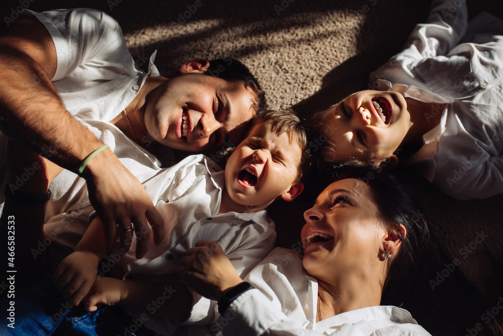 Happy family dressed in jeans and white shirts lie on the floor and laugh together in sunlight. Happy family dressed in jeans and white shirts lie on the floor and laugh together in sunlight.