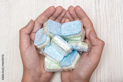 Hands holding many green and blue dishwasher soap tablets in water-soluble packaging