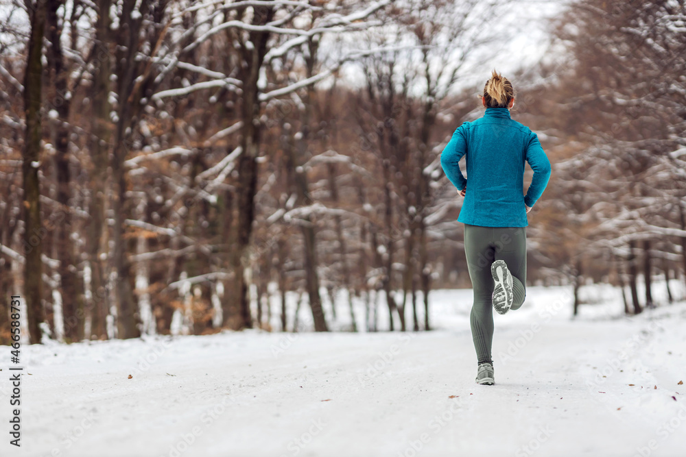 Rear view of sportswoman jogging in nature on a snowy weather. Cold weather, snow, healthy life, fitness, healthy habits