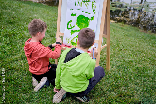 Children learn to paint on canvas, easel with paper. Boy artist paints nature and trees by the water surface of the river © Андрей Журавлев