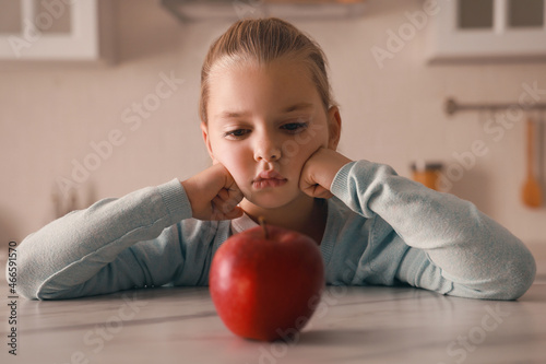 Cute little girl refusing to eat apple in kitchen photo