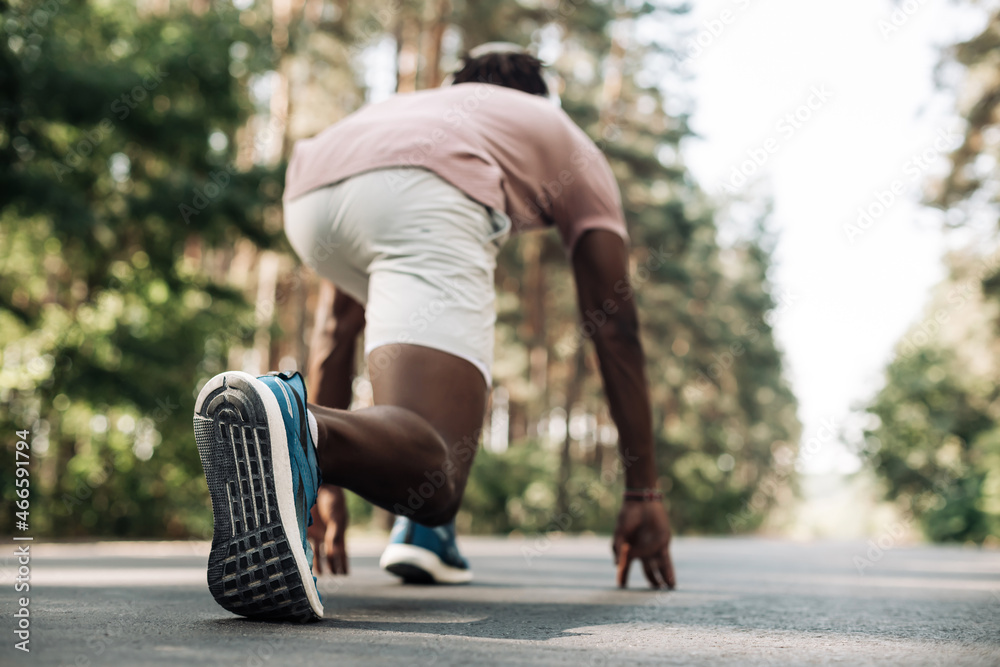 Obraz premium black male sprinter, in starting position ready to run, Male athlete about to start sprint outdoors in the park