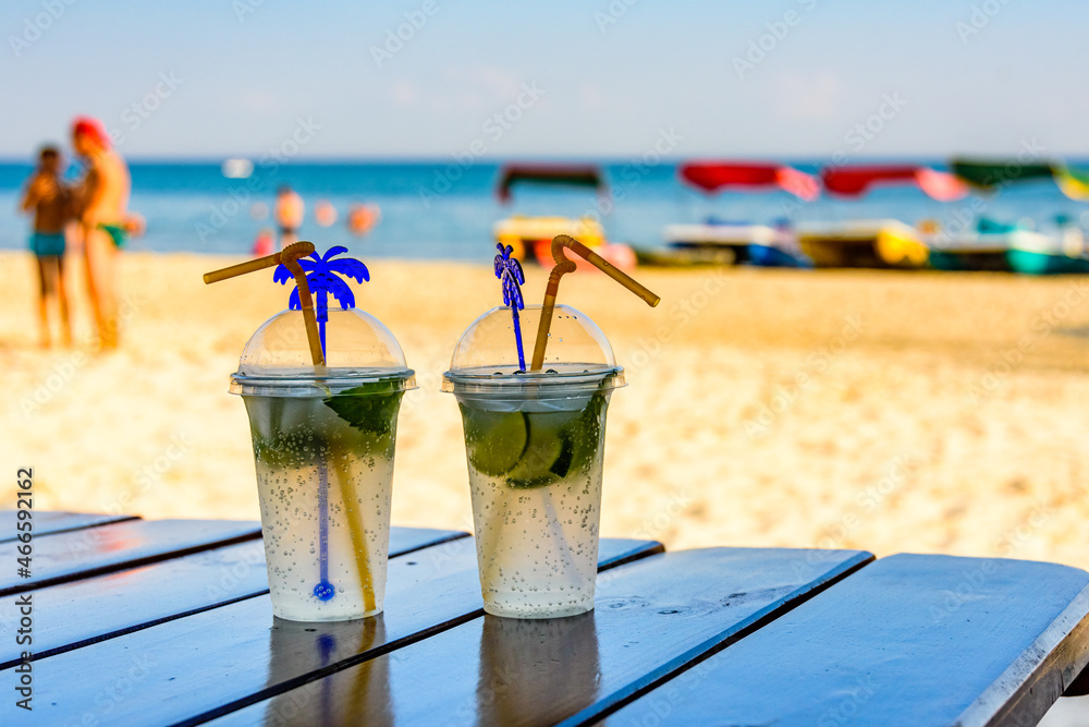 Two mojito cocktails on wooden table with sandy beach on a background Two mojito cocktails on wooden table with sandy beach on a background