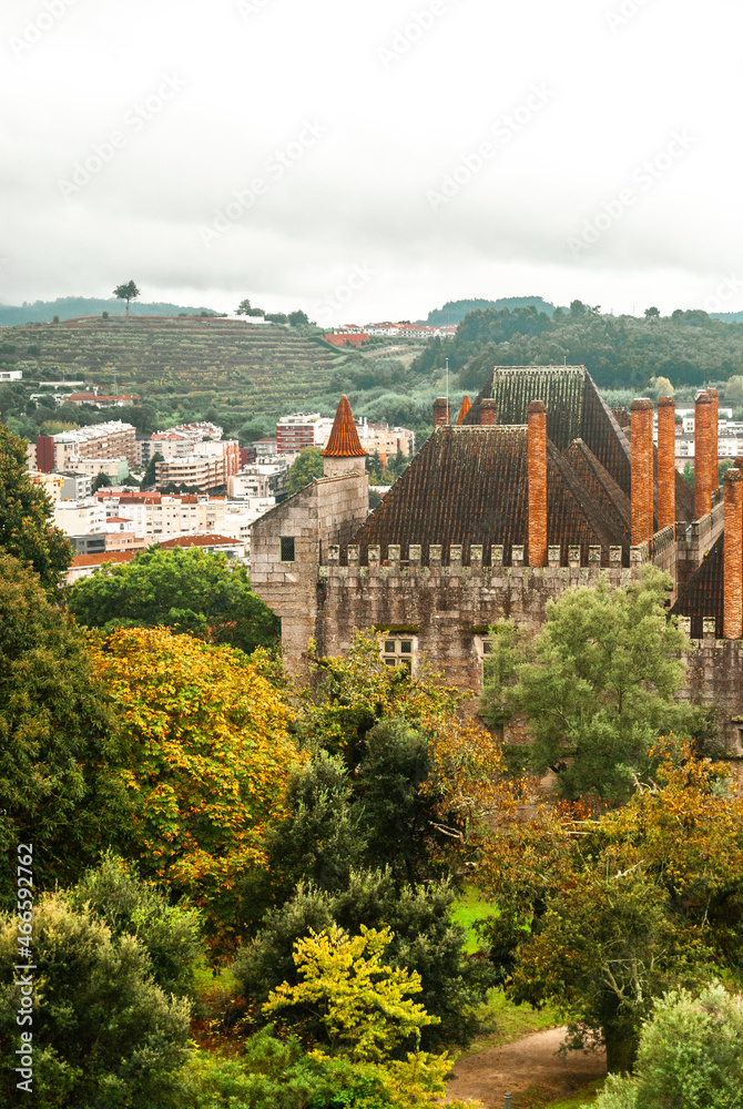 Palace in the autumn yellow orange and green forest with cloudy sky atmosphere of fall city in the background - Palace of Dukes in Guimaraes, Portugal