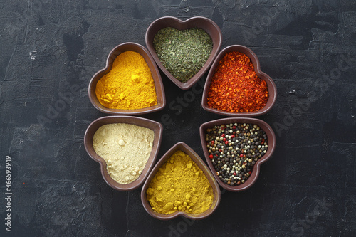Fototapeta Naklejka Na Ścianę i Meble -  Different kind of spices on a black stone. Oriental spices in in heart shaped bowl, red peppers, curry powder, cinnamon powder, mint powder, colorful peppers. Flat lay, top view.