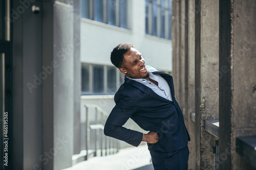 Businessman has severe back pain at work, african american freelancer man near office holding his back depressed trying to do massage