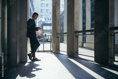 Male businessman near office reads news from tablet computer  african american freelancer in business suit near office outside